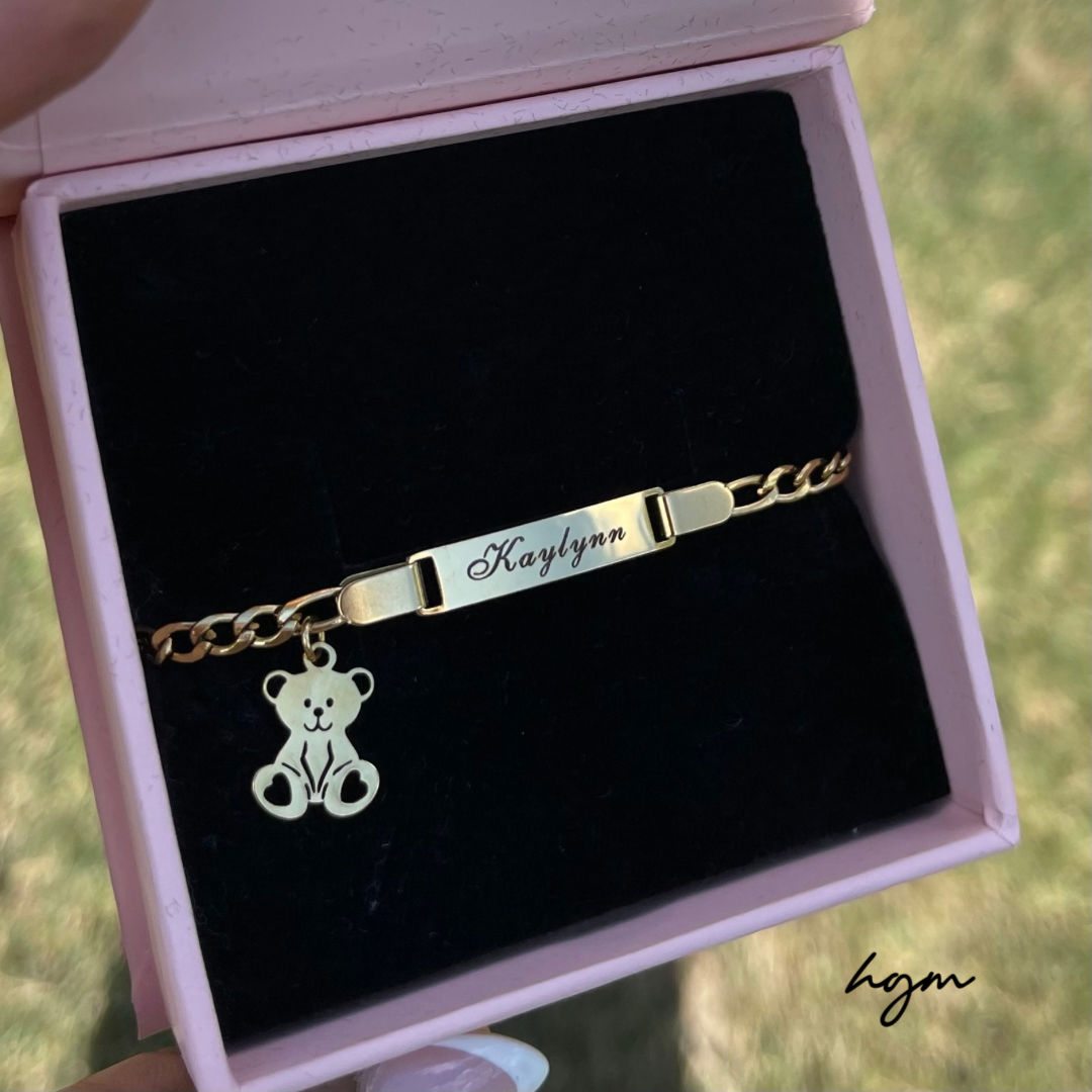 Personalized kids gold bracelet with engraved nameplate and teddy bear charm, displayed in a pink jewelry box – custom children’s jewelry gift.